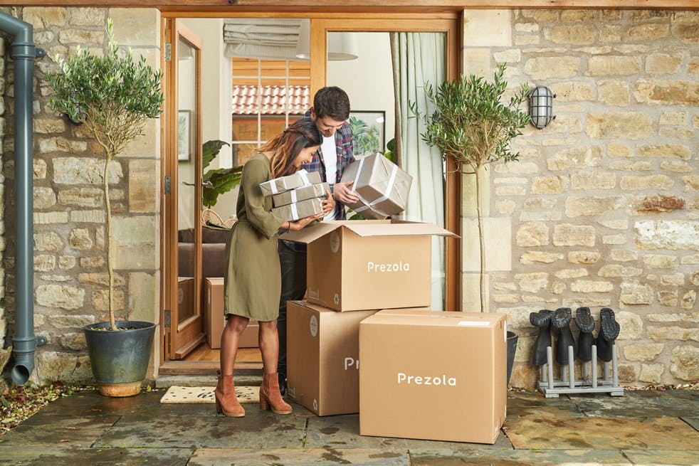 Woman and man stood outside a house looking through a pile of boxes with the word 'Prezola' written on them