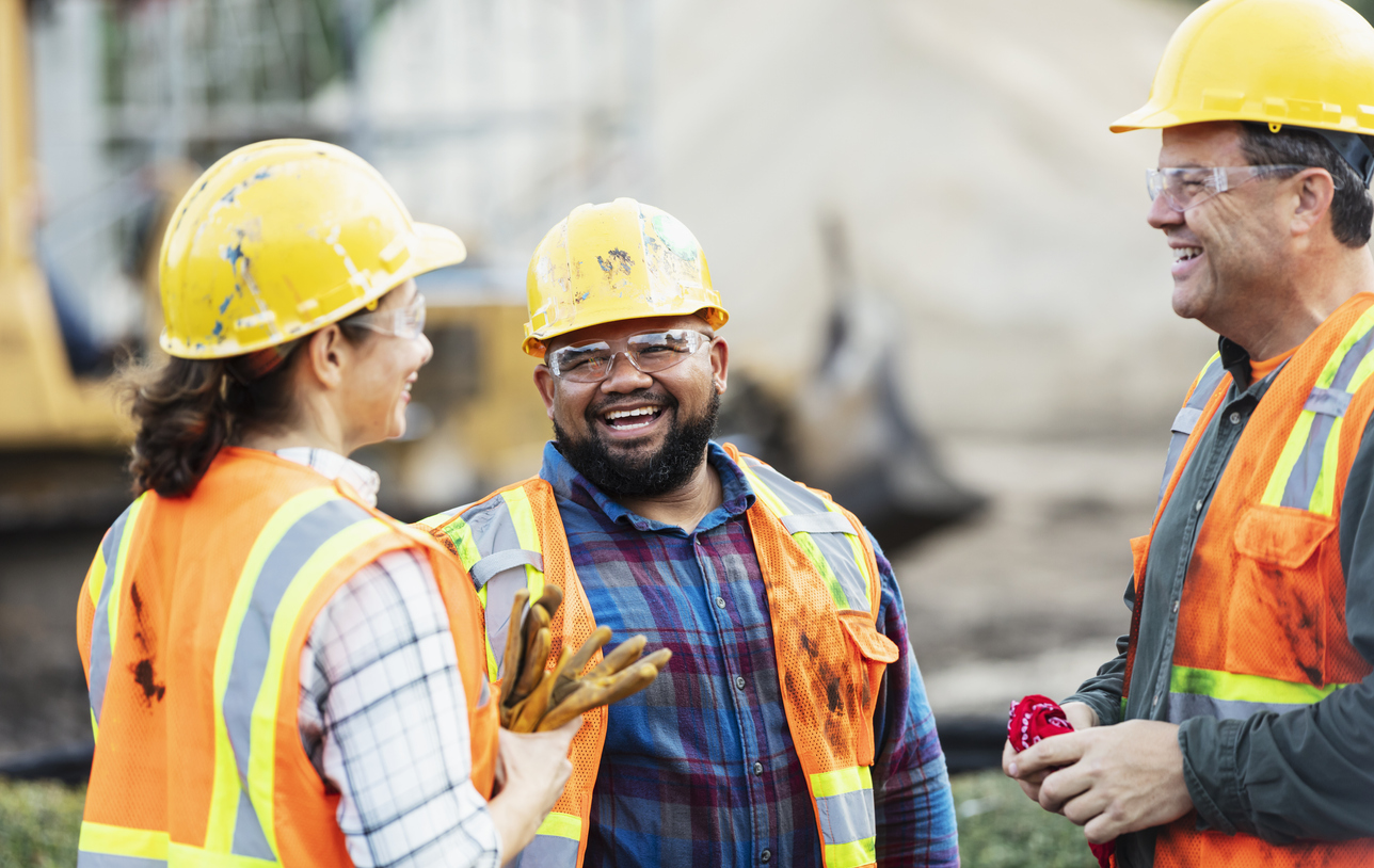 3 individuals, two men and one woman, wearing high vis jackets and hard hats standing in a circle laughing
