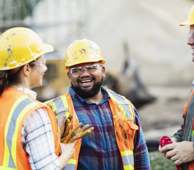 3 individuals, two men and one woman, wearing high vis jackets and hard hats standing in a circle laughing