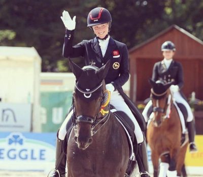 Laura Tomlinson riding one of her horses at a competition and waving to the crowd.